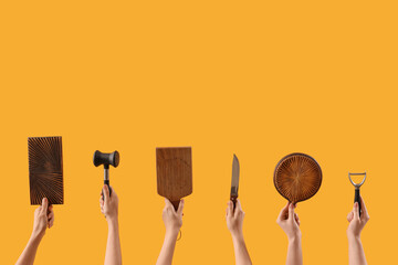 Female hands holding cutting board and different kitchen utensils on yellow background