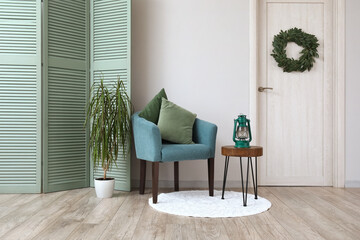 Interior of living room with blue armchair, folding screen, houseplant and stool
