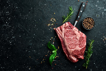 Raw marbled ribeye steak. Fresh meat and spices. Top view On a black stone background. Rustic style.