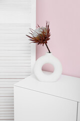 White chest of drawers with protea flower and folding screen near pink wall in room, closeup