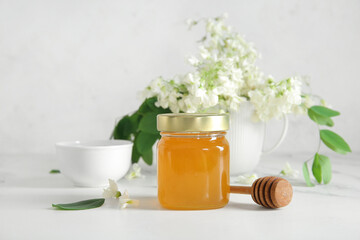 Bowl and jar of honey with flowers of acacia on light background, closeup