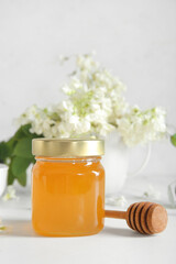 Jar of honey with flowers of acacia and dipper on light background, closeup