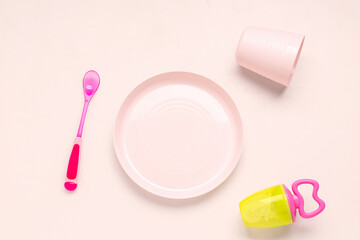 Plate with spoon, cup and nibbler for baby on pink background