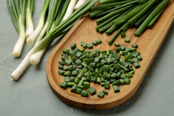 Board with slices of fresh green onion on grey background