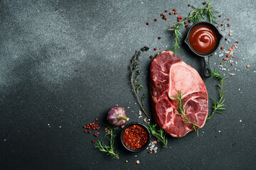 Raw ossobuco steak with rosemary and spices on a black stone background. Free space for text.