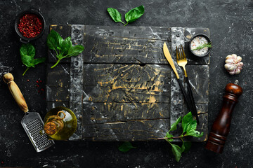 Cooking background: cutlery, spices and basil. On a black stone background.