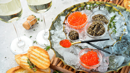A set of black and red caviar in glass bowls on a metal tray with ice. On concrete texture...