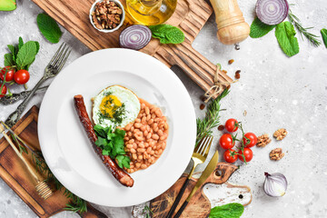 Breakfast. Eggs with sausage and beans. On a white plate. On a gray stone background. Restaurant menu.