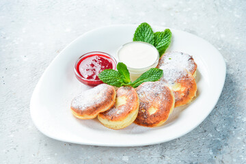breakfast Cheese pancakes with sour cream, jam and mint. On a white plate. On a gray stone background. Restaurant menu.