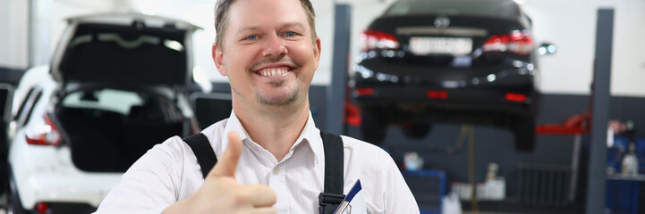 Portrait of young handsome man in uniform with thumbs up on background of car service....