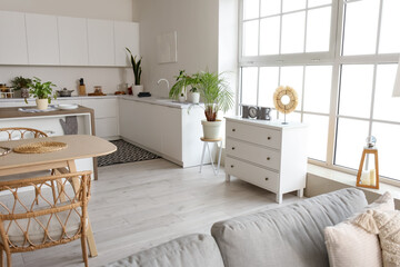 Fototapeta premium Interior of light open plan kitchen with grey sofa and chest of drawers