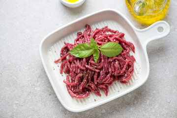 Beige serving tray with raw beef mincemeat and basil, high angle view on a beige stone background, horizontal shot