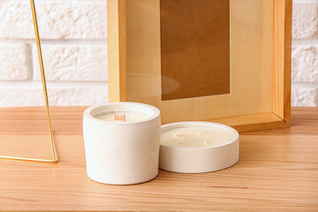 Holders with candles and frame on table near light brick wall in room, closeup