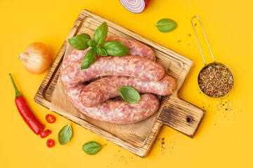 Board with raw fresh sausages and spices on orange background
