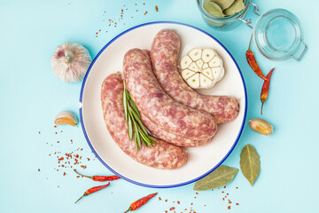 Plate with raw fresh sausages and spices on blue background