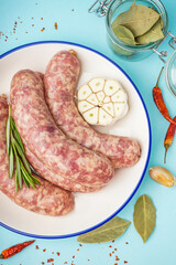 Plate with raw fresh sausages and spices on blue background