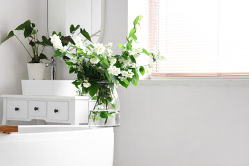Vase with blooming jasmine flowers on bathtub in interior of light bathroom
