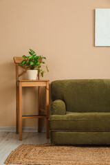Cozy grey sofa and houseplant on stool near beige wall