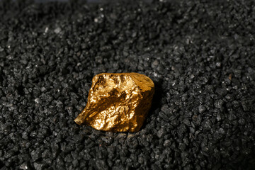 Golden nugget on black coal, closeup