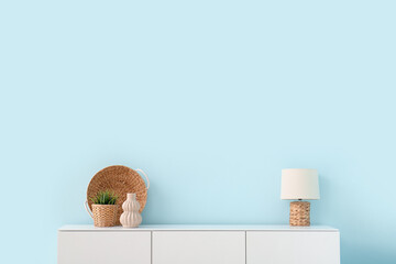 Modern chest of drawers with houseplant, lamp and decor near blue wall in room