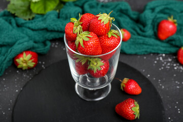 Board with glass of fresh strawberries on black background