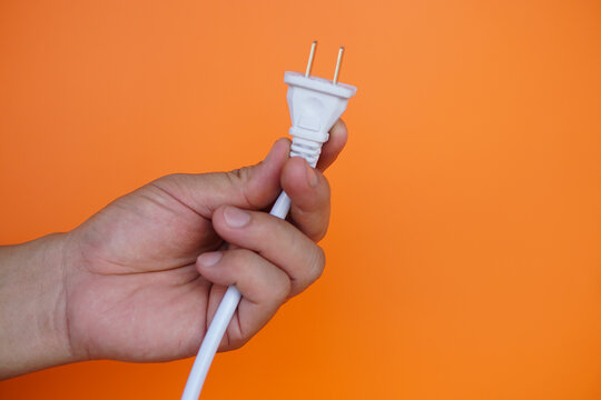 Close-up of male hand holding electric plug cable , orange background. Concept, save electricity  power. Campaign to plug off everytime after finish using electric appliances.  