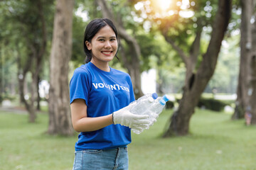 A group of happy young Asian volunteers in uniform stand in a public park with plastic garbage bags, helping their community by cleaning up an area in the park. - Powered by Adobe