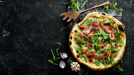 Traditional pizza with prosciutto, cherry tomatoes, arugula and cheese. Takeaway food. On a black...