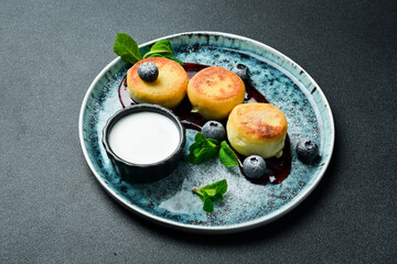Cheese pancakes with blueberries and sour cream. Dessert. On a dark background, close-up.