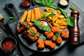 Beer snack plate: chicken nuggets, chicken wings, cheese and fries. On a dark background, close-up.