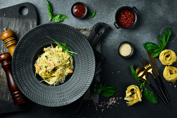 Pasta with pesto sauce and chicken in a black bowl. On a dark background, close-up.
