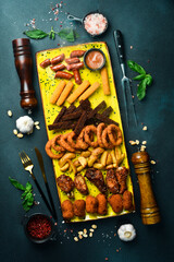 Appetizers for beer: onion rings, chicken nuggets, chicken wings, cheese fries. On a dark background, close-up.
