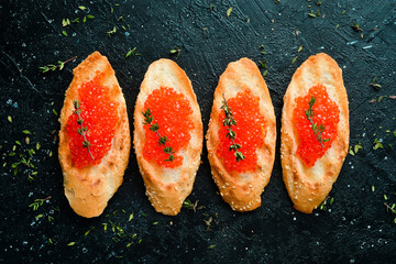 Toasts with red caviar on a stone plate, caviar in a bowl. On a black stone background. Rustic...