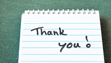 tank you written on white notepad or writing pad with blue lines on green background as gratitude,...