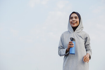 Fototapeta premium asian muslim woman running and exercising while holding drink bottle outdoors excitedly