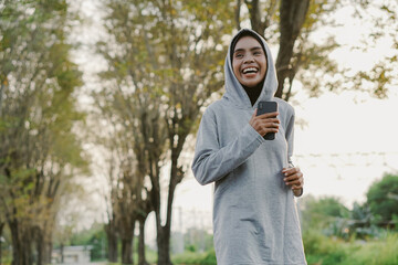 Fototapeta premium asian muslim woman running and exercising while holding mobile phone outdoors excitedly