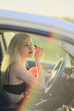 The woman behind the wheel is painting her eyelashes. Blond woman in the car applying makeup