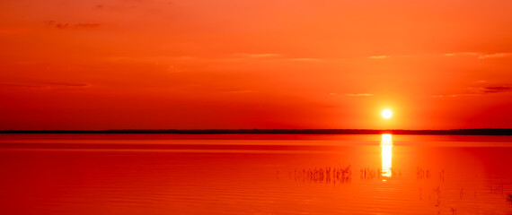 Beautiful red sunset above the lake. Sun path. Seascape. Calm water. Natural background. Bright orange color. Nature landscape. Summertime travelling. Sunny weather. Warm evening concept. No people