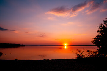 Beautiful sunset above the lake with blue sky and rare fluffy pink clouds. Sun path. Seascape. Calm water. Natural background. Nature landscape. Summertime travelling. Warm evening concept. No people