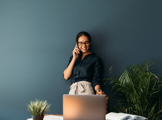 Young business woman smiling and looking down while learning blue wall taking on mobile phone