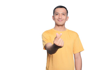 Smiling young Asian man wearing yellow t-shirt showing Korean heart love sign isolated on white background.