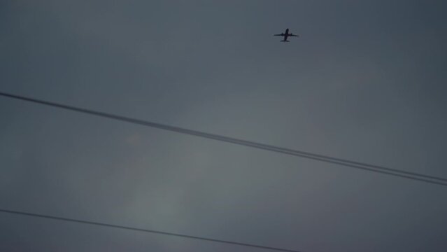 Low angle shot of an airplane flying in the twilight sky over parallel power lines
