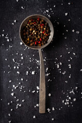 Big old spoon with peppercorn and salt pile on black background