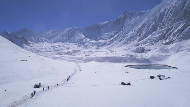 Aerial panning view group of trekkers on famous Tilicho lake trek with tiny alpine lake background. Nepal popular treks. Himalayas tours and mountains trekking concept