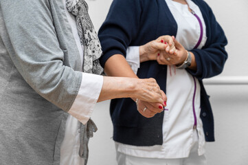 Nurse helping elderly woman walk in the room, holding his hand, supporting her. Treatment and rehabilitation after injury or stroke, life in assisted living facility, senior care concept.