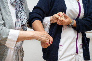 Nurse helping elderly woman walk in the room, holding his hand, supporting her. Treatment and rehabilitation after injury or stroke, life in assisted living facility, senior care concept.