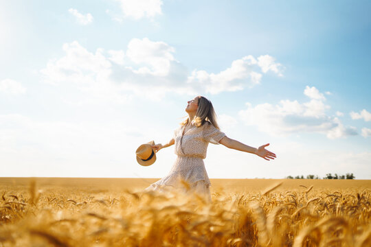 Stylish young woman in a summer dress and hat posing in a golden wheat field. Fashion, glamour, lifestyle concept. - Powered by Adobe