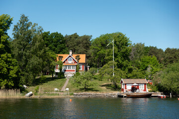 Fototapeta na wymiar Typical Swedish red house with white trims by sea shore in idyllic summer landscape 