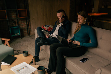 Long hair bearded businessman having a phone call while working on the tablet. His female coworker is having a meeting with new clients