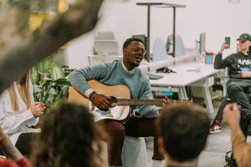 A good looking black male person playing guitar and singing song for his colleagues - Powered by Adobe